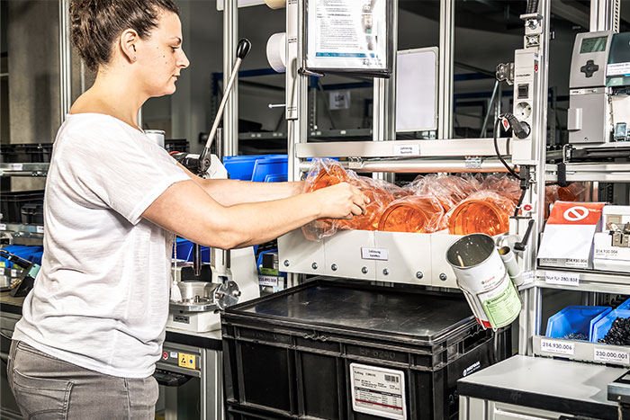 Mitarbeiterin an der Produktionslinie erhält durch das Kanban-System Materialnachschub exakt zur richtigen Zeit.