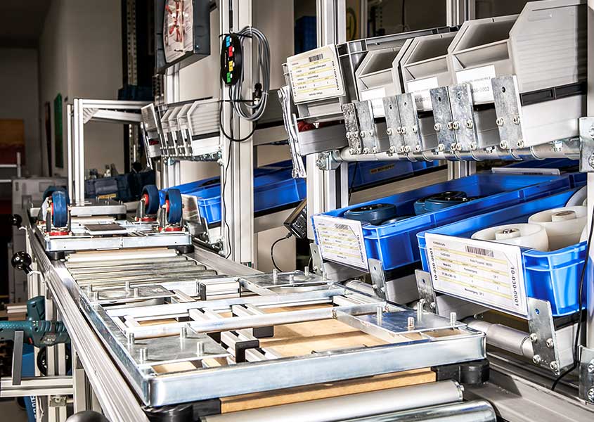 Montagearbeitsplatz mit E-Kanban-System, das Material nachschiebt, um Lagerbestände niedrig zu halten und die Produktion kontinuierlich zu versorgen