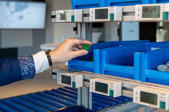 Frau entnimmt ein C-Teil aus einer KLT-Box am Werkerassistenzsystem – Beispiel für effizientes C-Teile-Management mit E-Kanban.