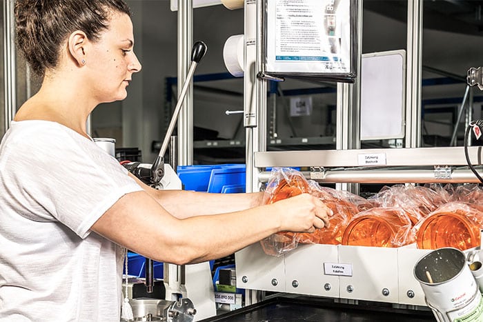 Mitarbeiterin entnimmt Teile aus einem Pufferregal, das durch ein Kanban-System digital gesteuert wird.